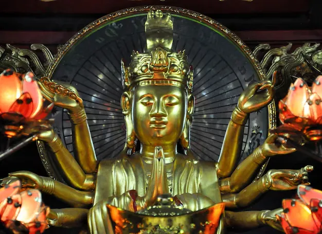 Golden many-armed Avalokitesvara bodhisattva statue in a pagoda shrine framed by glowing lotus-shaped lamps
