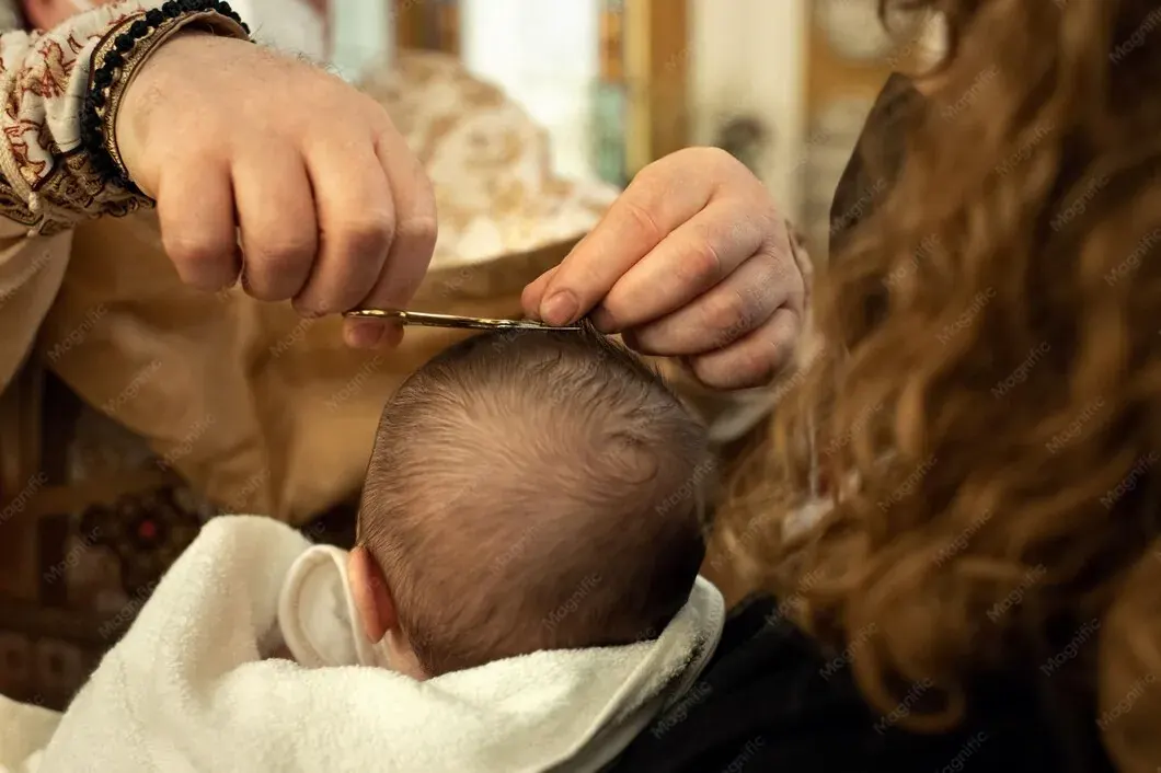 Baby wrapped in a white towel having a first haircut as an adult snips a lock of hair with scissors