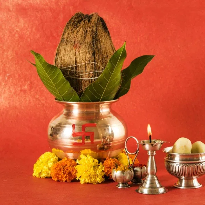 Copper kalash topped with a coconut and mango leaves, marked with a red swastika, surrounded by marigold flowers and a lit oil lamp