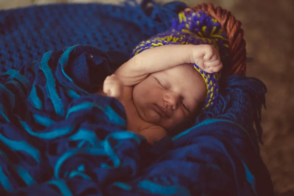 Sleeping newborn in a knitted blue and yellow cap wrapped in a blue blanket for the Namakarana baby naming ceremony