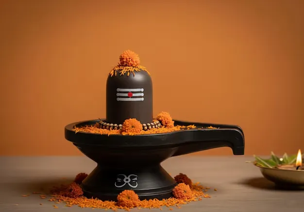 Black Shiva lingam decorated with a marigold garland and orange flowers beside a small lit lamp
